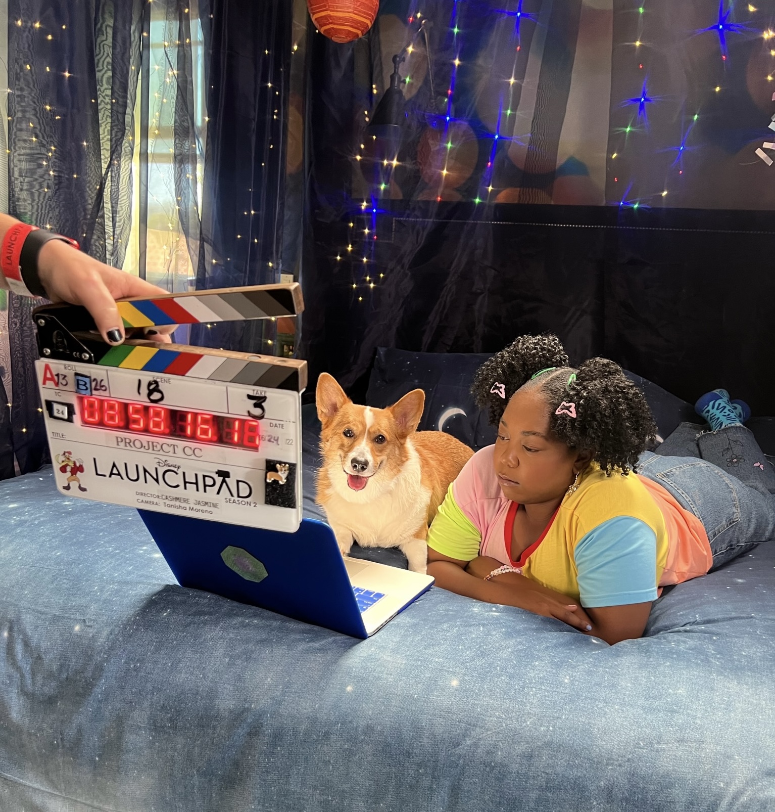 Red & white corgi acting dog lying down on a bed with a young actress while filming the Disney movie 'Launchpad"